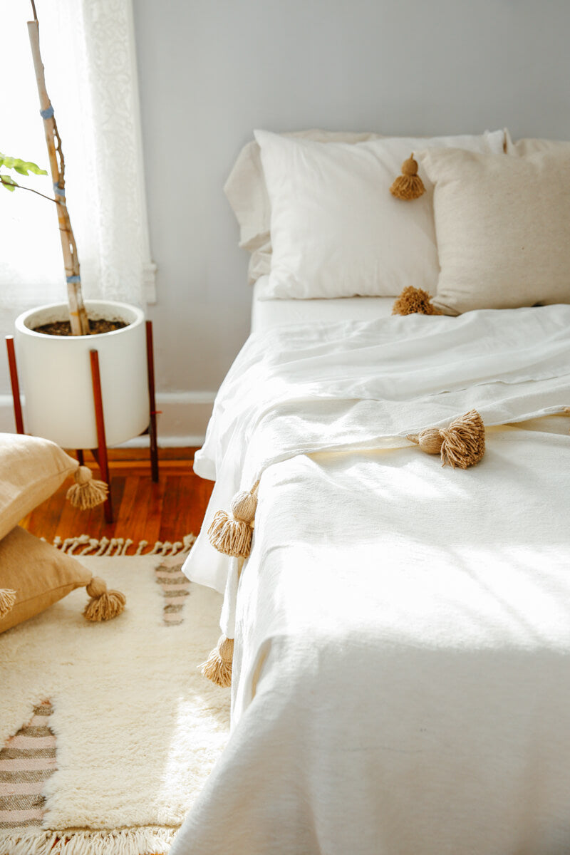 Moroccan Pom Pom Blanket - White with Beige Pom-poms styled on Bed with rug and pillows