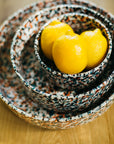 A set of three multicolor teal ceramic splatter paint nesting bowls, with one bowl containing a lemon slice, on a wooden surface.