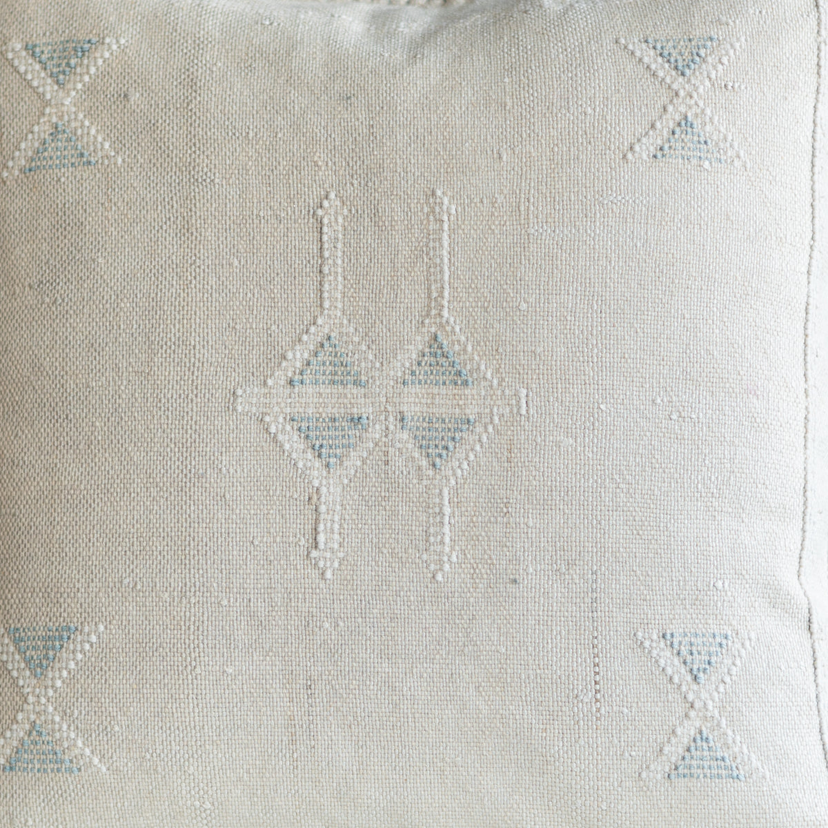 Close-up of a textured off-white woven fabric with a geometric embroidered pattern in light blue and off-white.