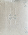 Close-up of a textured off-white woven fabric with a geometric embroidered pattern in light blue and off-white.