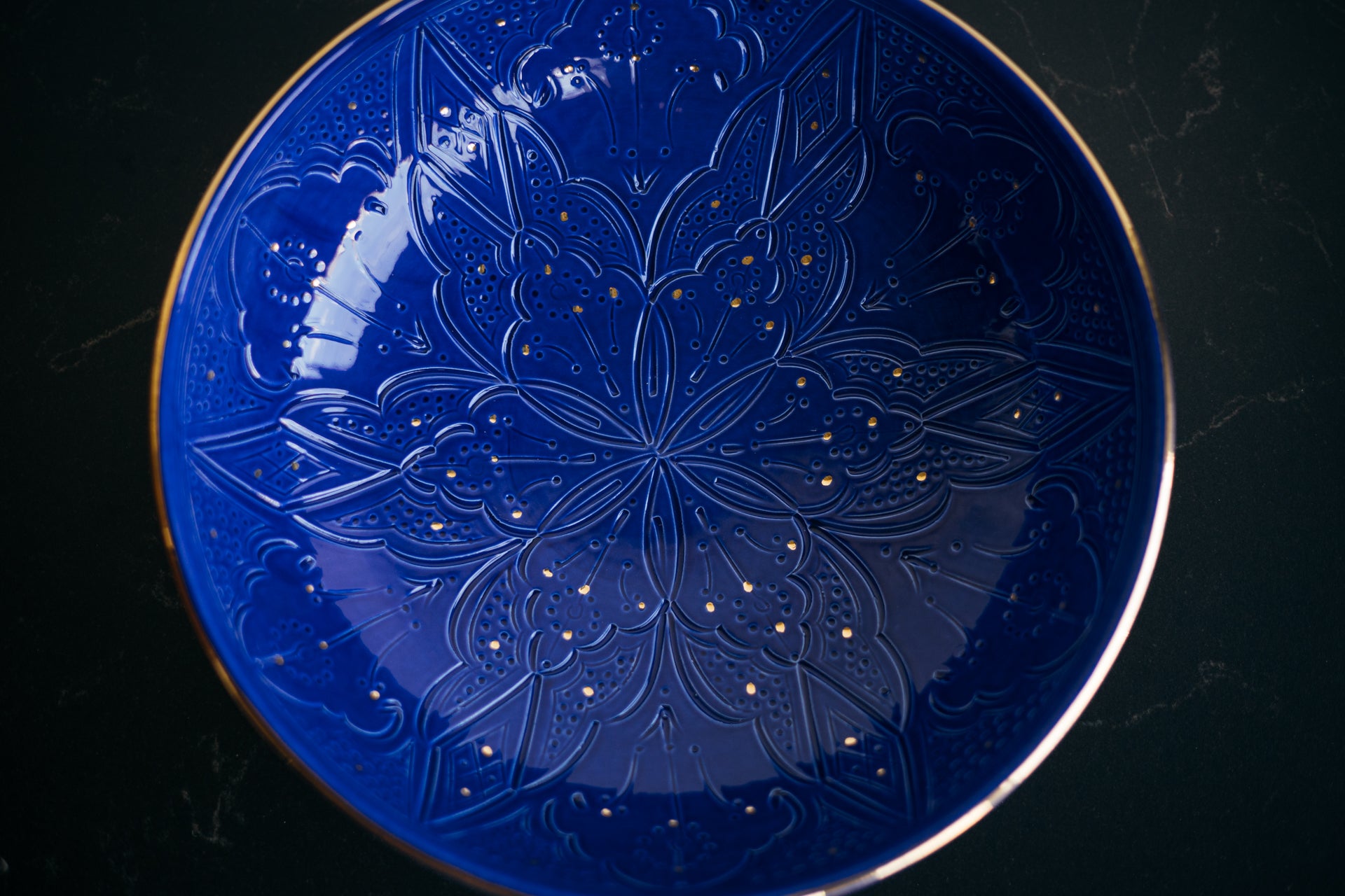 Blue ceramic plate with traditional Moroccan floral embossing on a black background