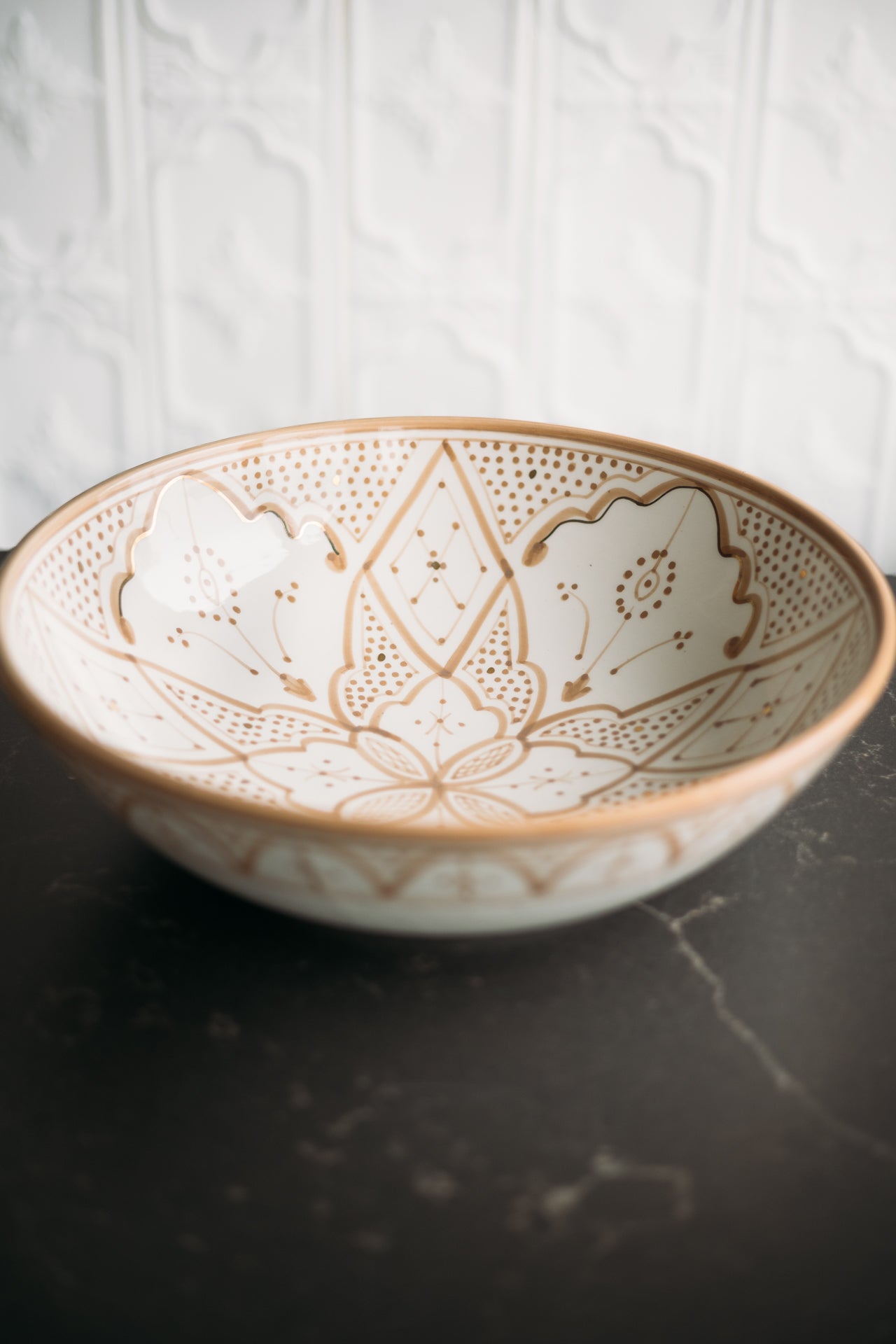 Decorative ceramic bowl with intricate hand painted tan patterns on a dark surface.