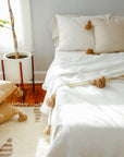 Moroccan Pom Pom Blanket - White with Beige Pom-poms styled on Bed with rug and pillows