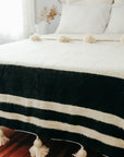 Moroccan Pom Pom Wool Blanket - Natural White with Black Stripes styled on bed